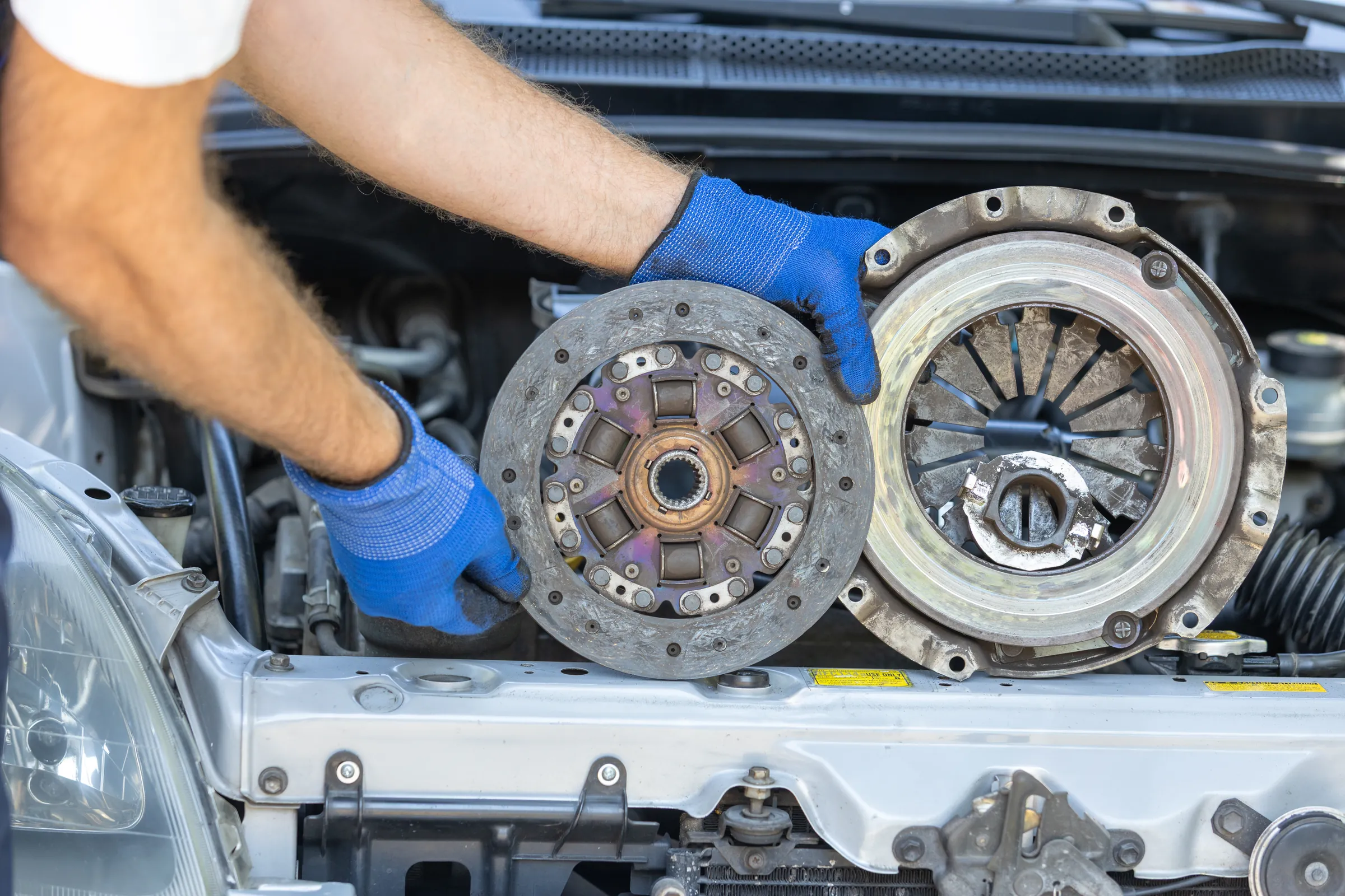 Technician holding a worn clutch disc and pressure plate for clutch replacement