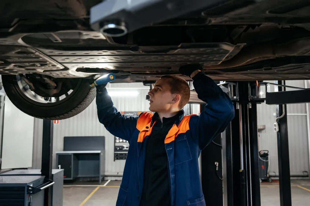 Technician using a flashlight to check for transmission fluid leaks under a vehicle
